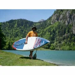 Göl kenarında şişme SUP board taşıyan adam, doğa ve su sporları ortamı