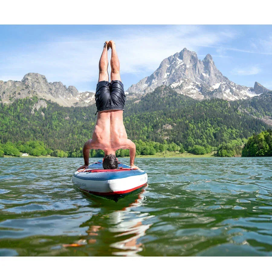 Dağ manzaralı gölde SUP board üzerinde başüstü duran adam, su sporları keyfi.