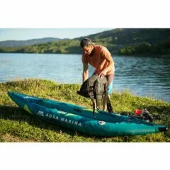 Gölden kıyıya çekilmiş şişme Aqua Marina kano, yanında eşyalarını toplayan bir kişi.