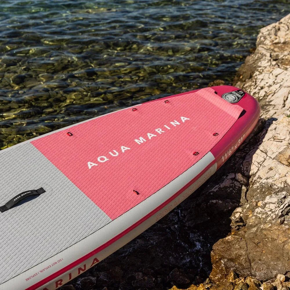 Kıyıda duran pembe gri Aqua Marina şişme SUP board, berrak su ve kayalıklar