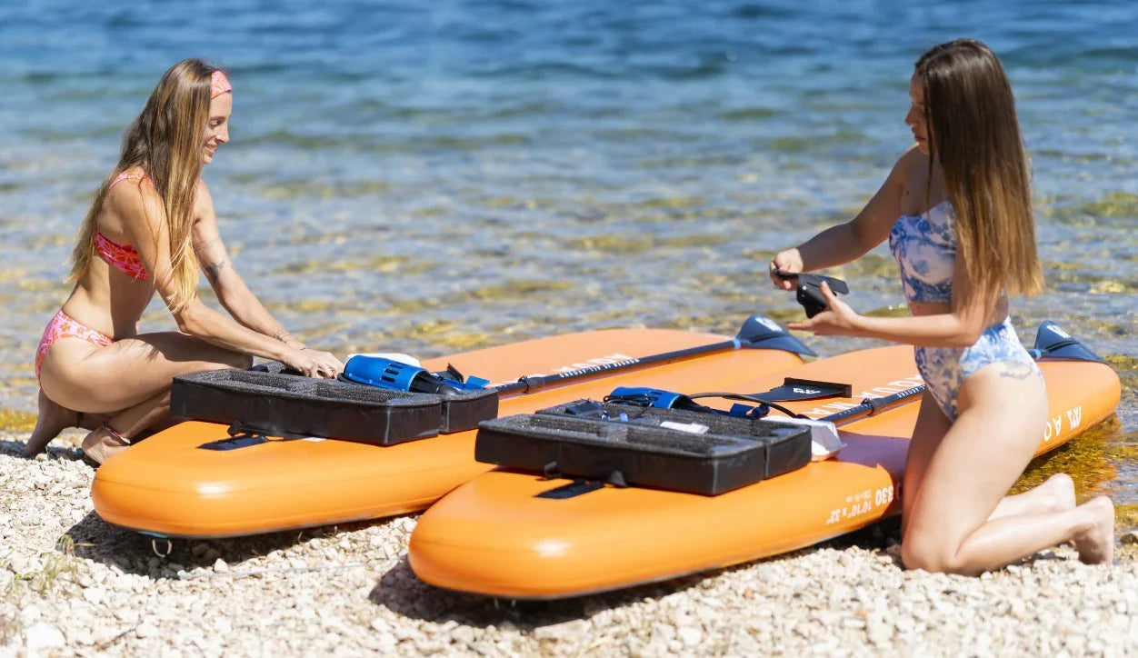 Göl kenarında turuncu şişme SUP board üzerine ekipman yerleştiren iki kadın