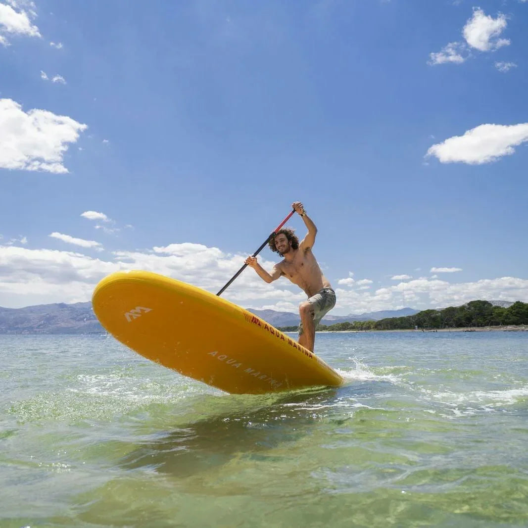 Denizde sarı SUP board üzerinde kürek çeken erkek, açık havada su sporu keyfi.