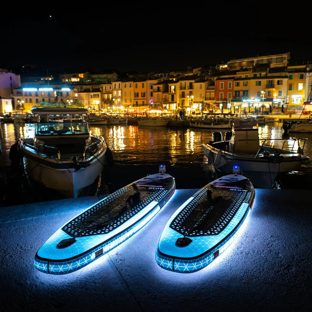 Gece limanda yanan ışıklı SUP boardlar, arka planda tekneler ve renkli binalar