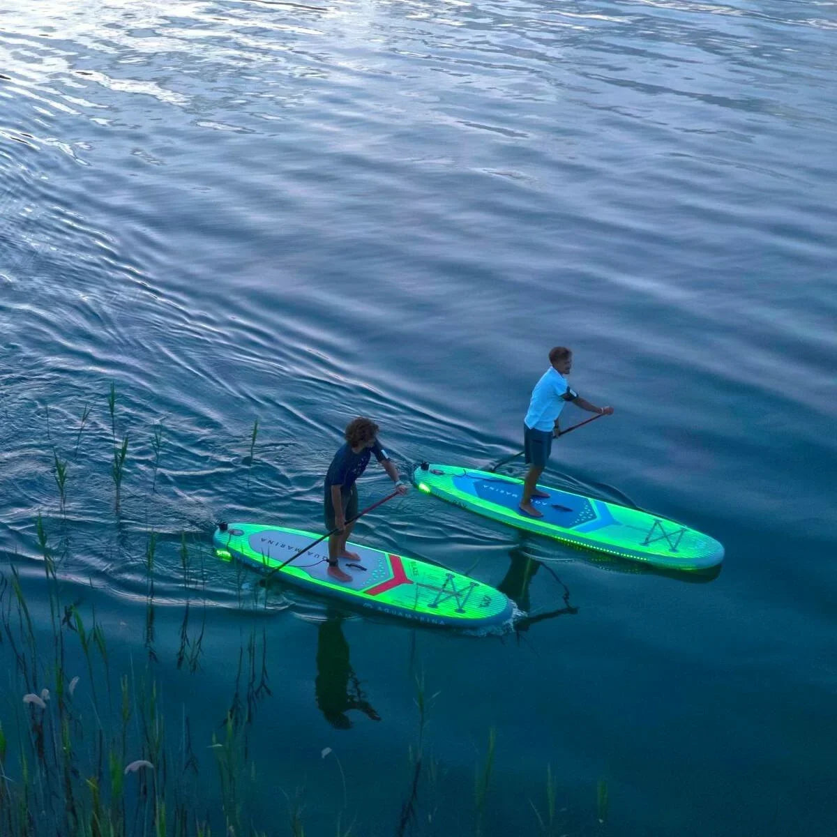 İki kişi gölde aqua marina şişme SUP board üzerinde kürek çekiyor.