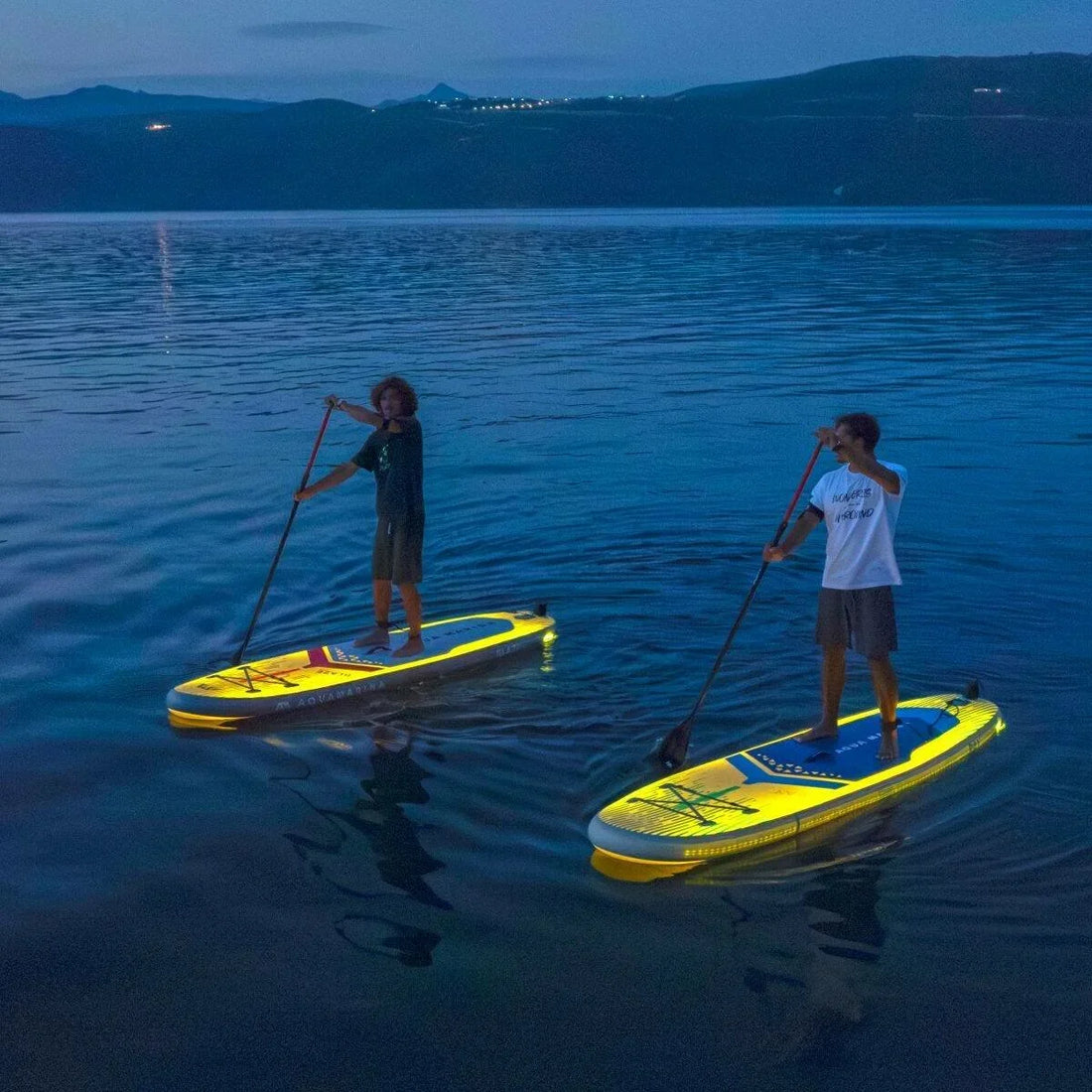 Gece su üzerinde Aqua Marina Ray SUP board ile kürek çeken iki kişi, LED aydınlatmalı paddle board keyfi.