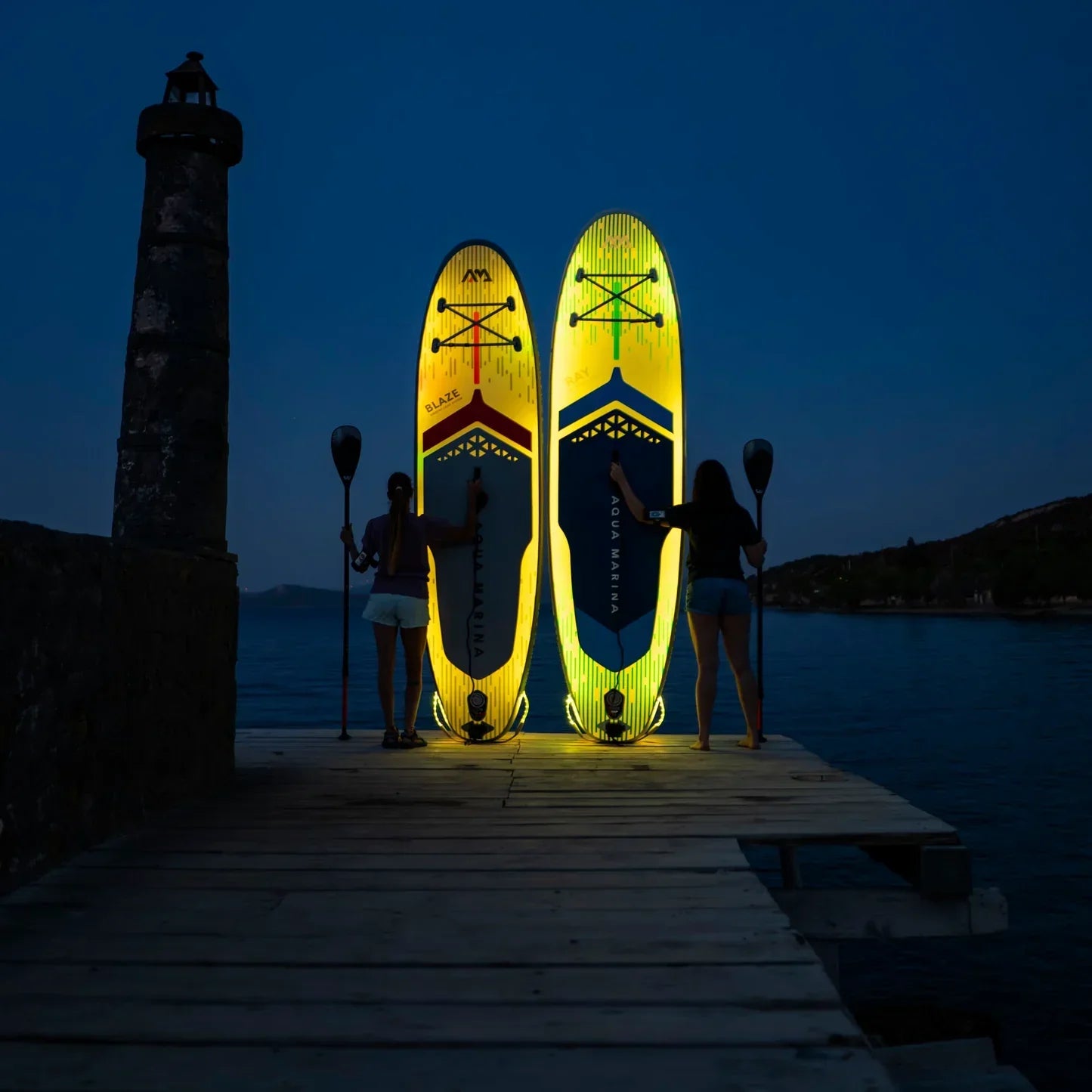 Gece iskelede, iki kadın Aqua Marina SUP board ile ayakta, su sporları ekipmanı
