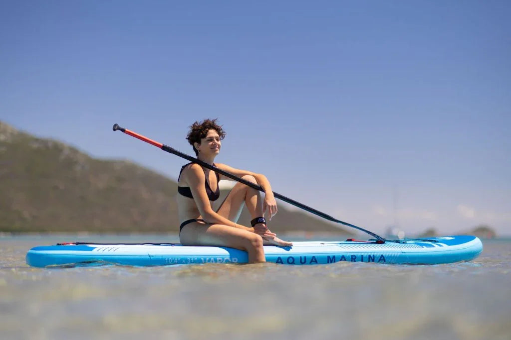 Denizde oturan kadın, mavi SUP paddle board ve kürekle açık havada su sporları