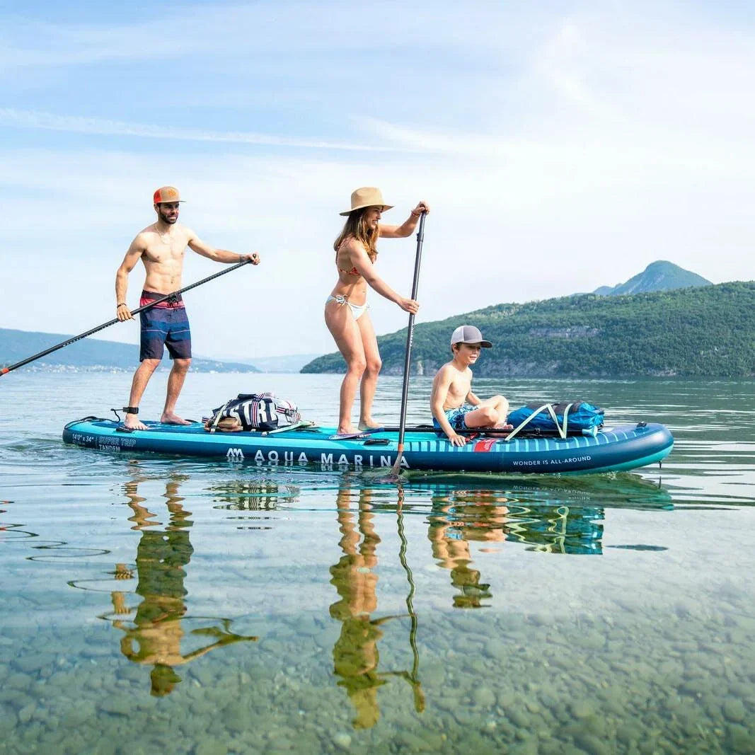 Gölde kürek sörfü yapan üç kişi, Aqua Marina şişme SUP board üzerinde, doğa manzaralı.